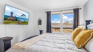 A bedroom with a large bed, a TV mounted on the wall, a window with curtains, and a view of the outdoors. - 203 Walk to The Landing & Convention Center (Branson)