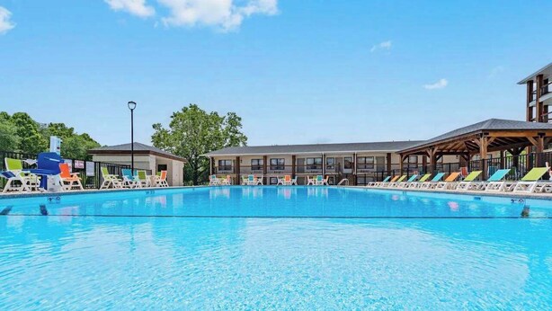 A swimming pool with lounge chairs and a building with multiple windows in the background. - 203 Walk to The Landing & Convention Center (Branson)