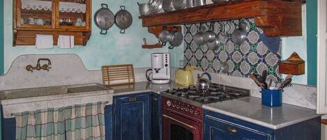 A vintage kitchen with a gas stove, wooden cabinets, and a tiled backsplash.
