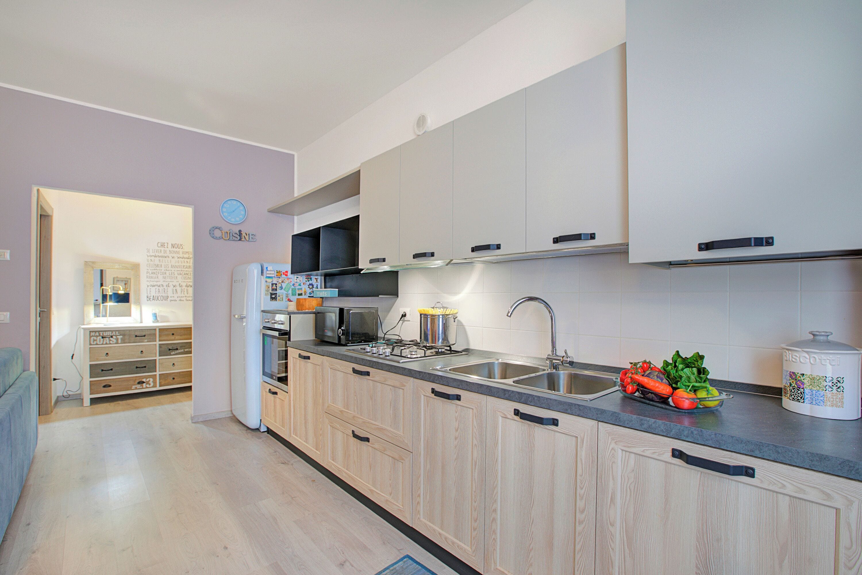 A modern kitchen with wooden cabinets, a microwave, a sink, and a countertop with fresh vegetables.