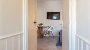 Ein Flur, der in einen Essbereich mit einem runden Tisch, einem Stuhl und einem an der Wand befestigten Fernseher führt.