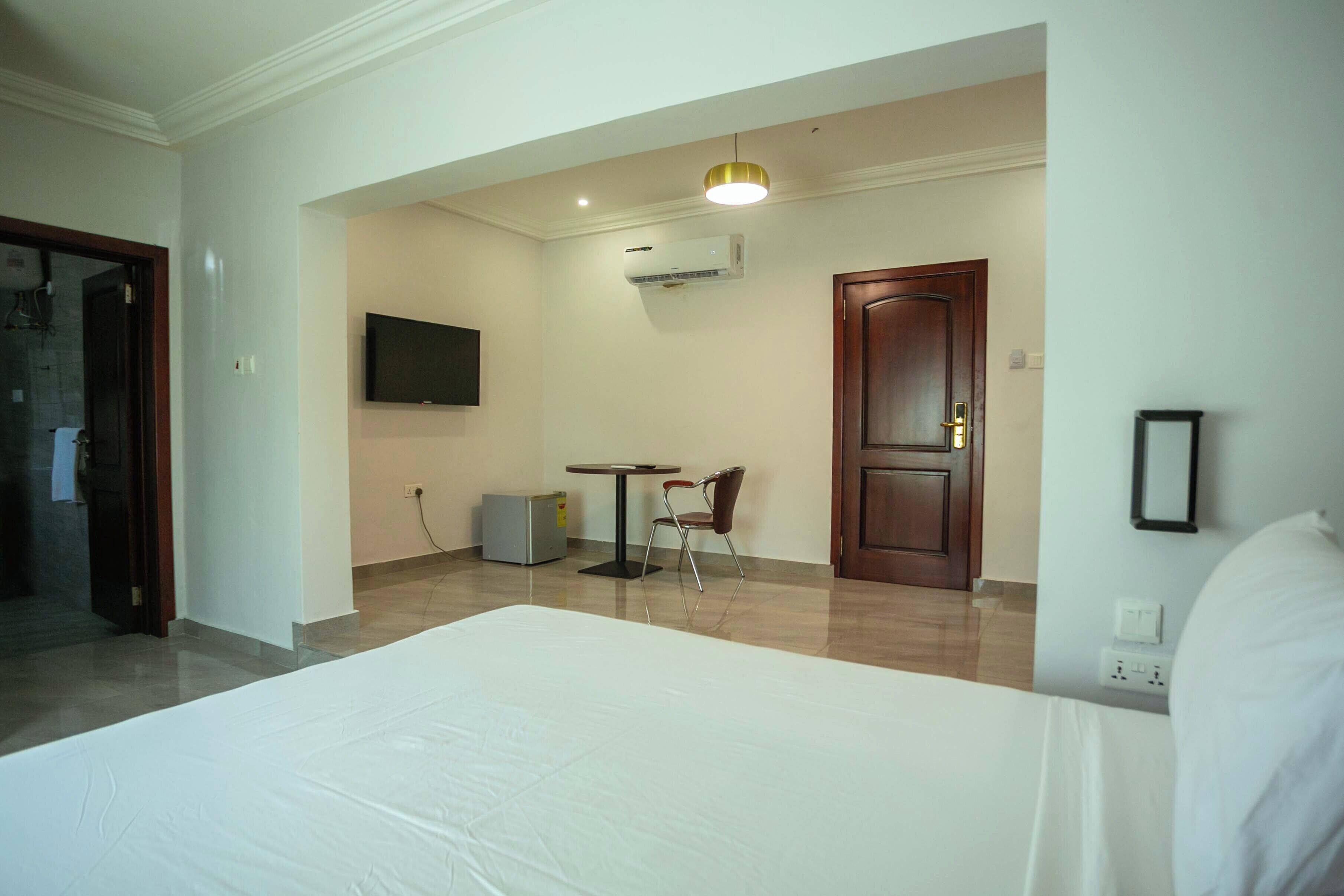 A hotel room with a bed, a desk, a chair, an air conditioning unit, and a television.