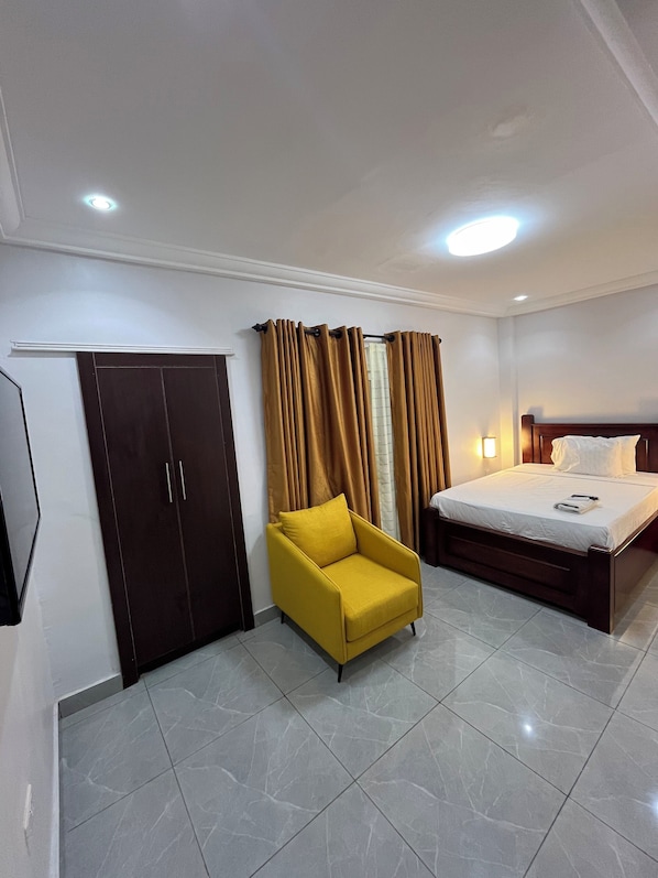 A hotel room with a bed, a yellow armchair, a wardrobe, and a flat-screen TV. - Aklin Hotel and Resorts (Accra)
