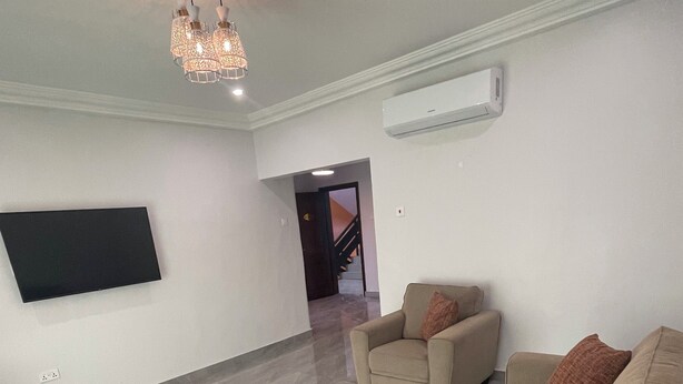 A spacious living room with a large beige sofa, a smaller armchair, and a flat-screen TV mounted on the wall. - Aklin Hotel and Resorts (Accra)