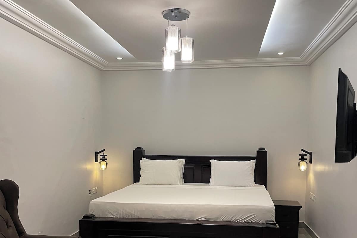 A modern bedroom with a large bed, two bedside tables, a chair, and a flat-screen TV mounted on the wall.