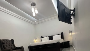 A modern hotel room with a large bed, a dark brown armchair, and a flat-screen TV mounted on the wall. - Aklin Hotel and Resorts (Accra)