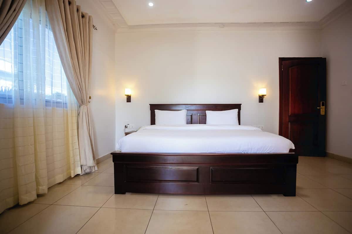 A neatly made bed in a hotel room with a wooden headboard, two bedside lamps, and a closed door.