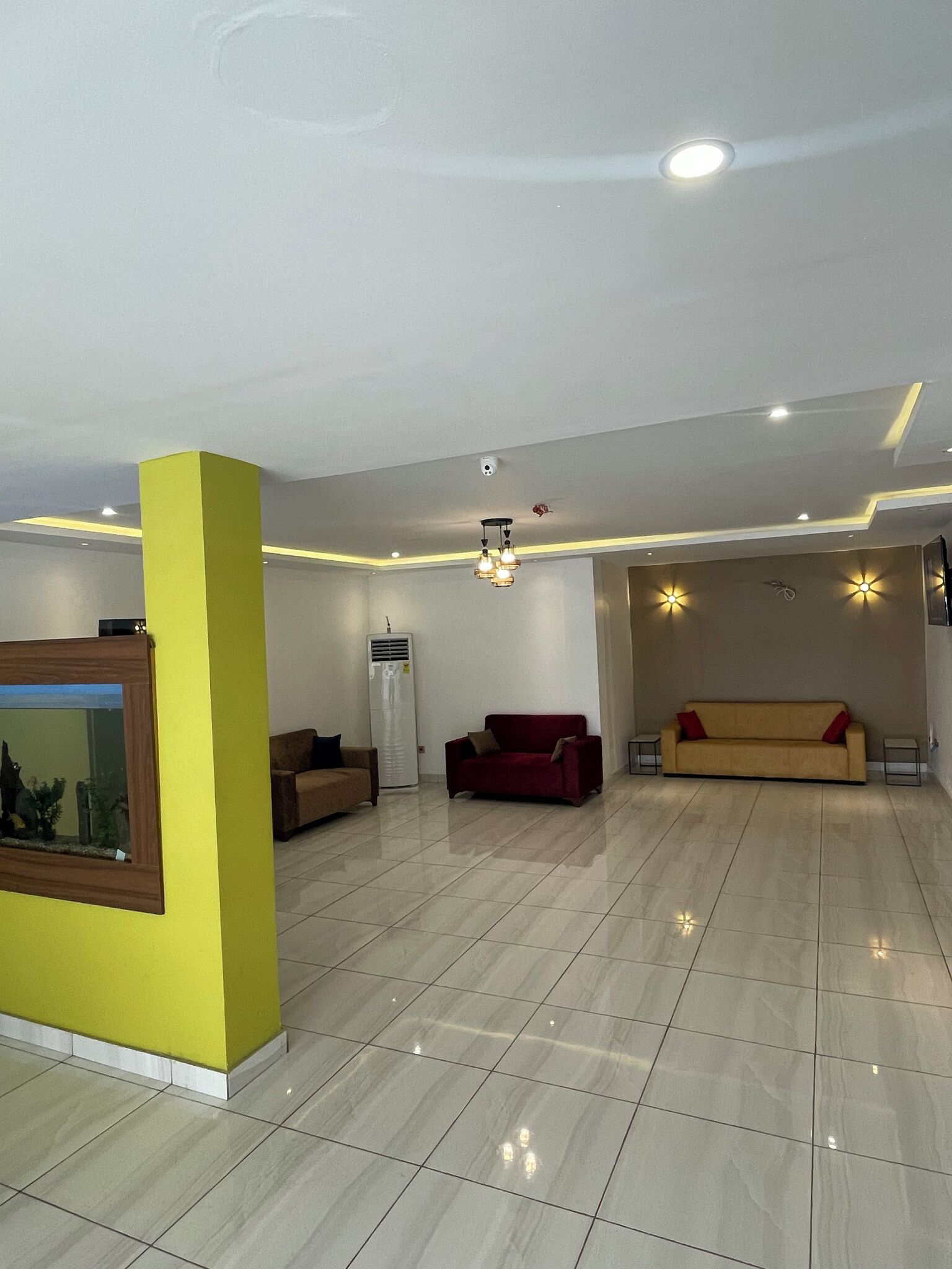 Una habitación amplia con una pared de acento amarilla, un espejo grande, un sofá rojo, un sofá beige e iluminación empotrada y luces decorativas en forma de estrella en el techo.