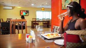 A dining area with wooden tables, chairs, and a television in the background. - Aklin Hotel and Resorts (Accra)