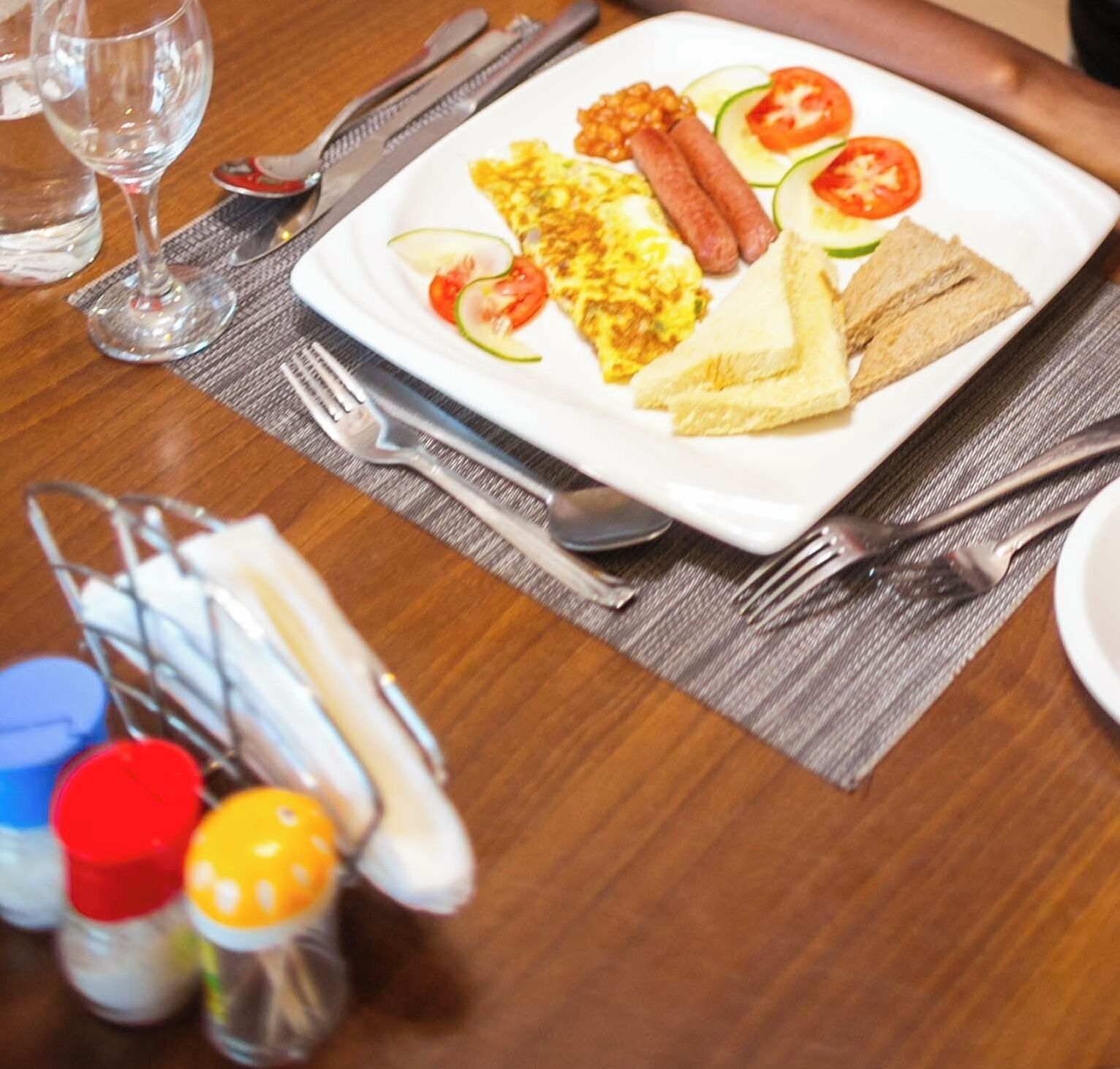 A breakfast plate with eggs, sausages, tomatoes, and toast on a wooden table.
