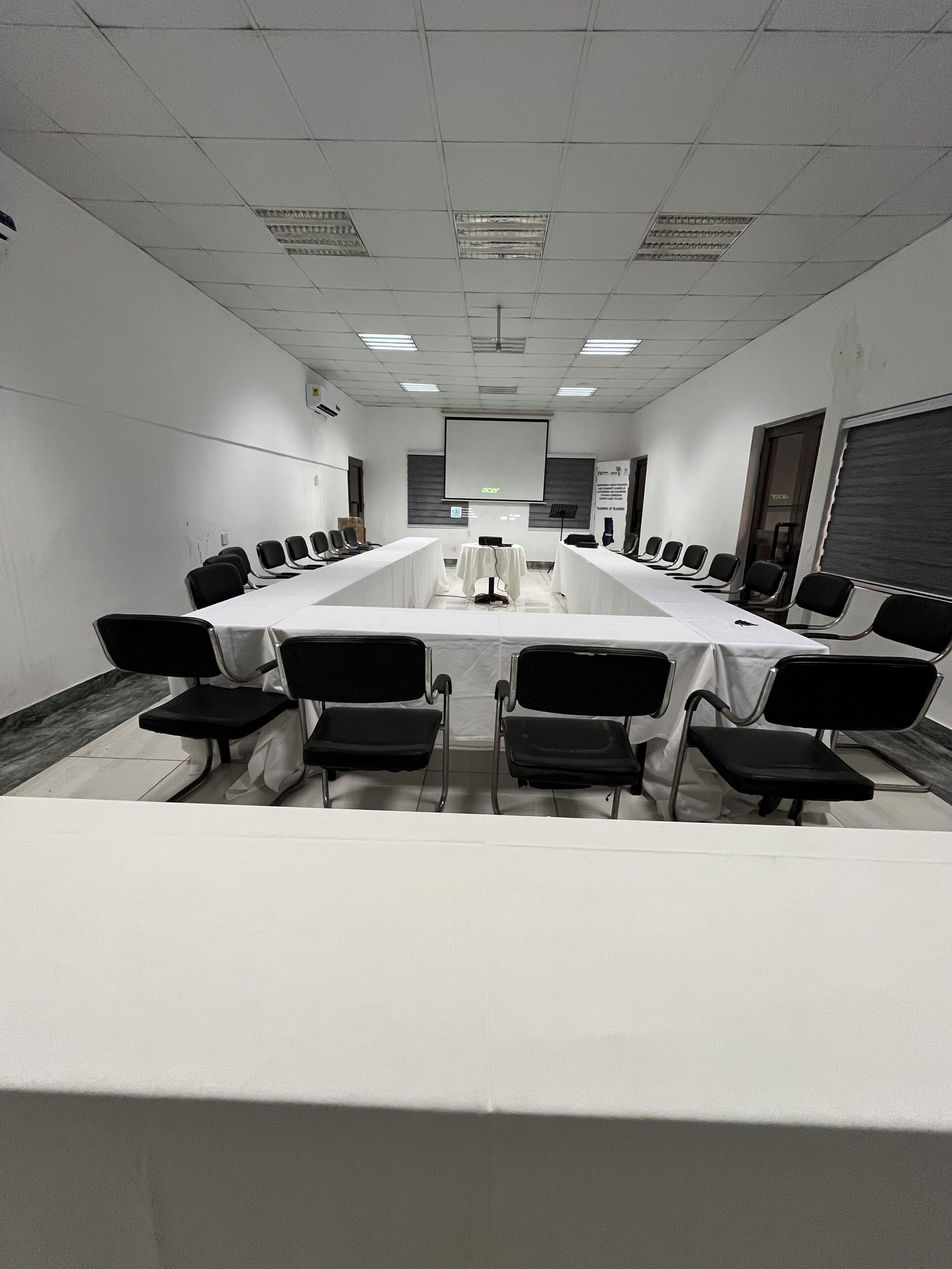 A conference room with a long table, chairs, a projector screen, and a whiteboard.