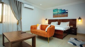 A hotel room with a bed, a sofa, a wooden table, and a painting on the wall. - Aklin Hotel and Resorts (Accra)