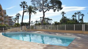 A swimming pool with a tiled deck, surrounded by palm trees and a white fence. - Charming seafront studio with terrace and pools in private residence (Saint-Raphaël)