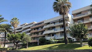 A multi-story residential building with balconies, surrounded by palm trees and greenery. - Charming seafront studio with terrace and pools in private residence (Saint-Raphaël)