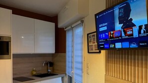 A modern kitchen with a flat-screen TV mounted on the wall, a wooden countertop, and pendant lighting. - Charming seafront studio with terrace and pools in private residence (Saint-Raphaël)