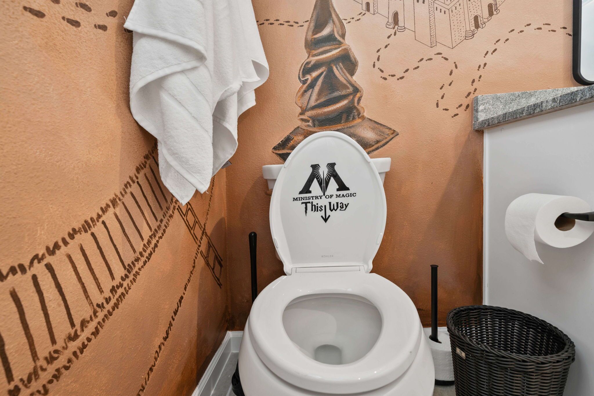 Une salle de bain avec des toilettes, une serviette blanche accrochée au mur et une fresque murale.