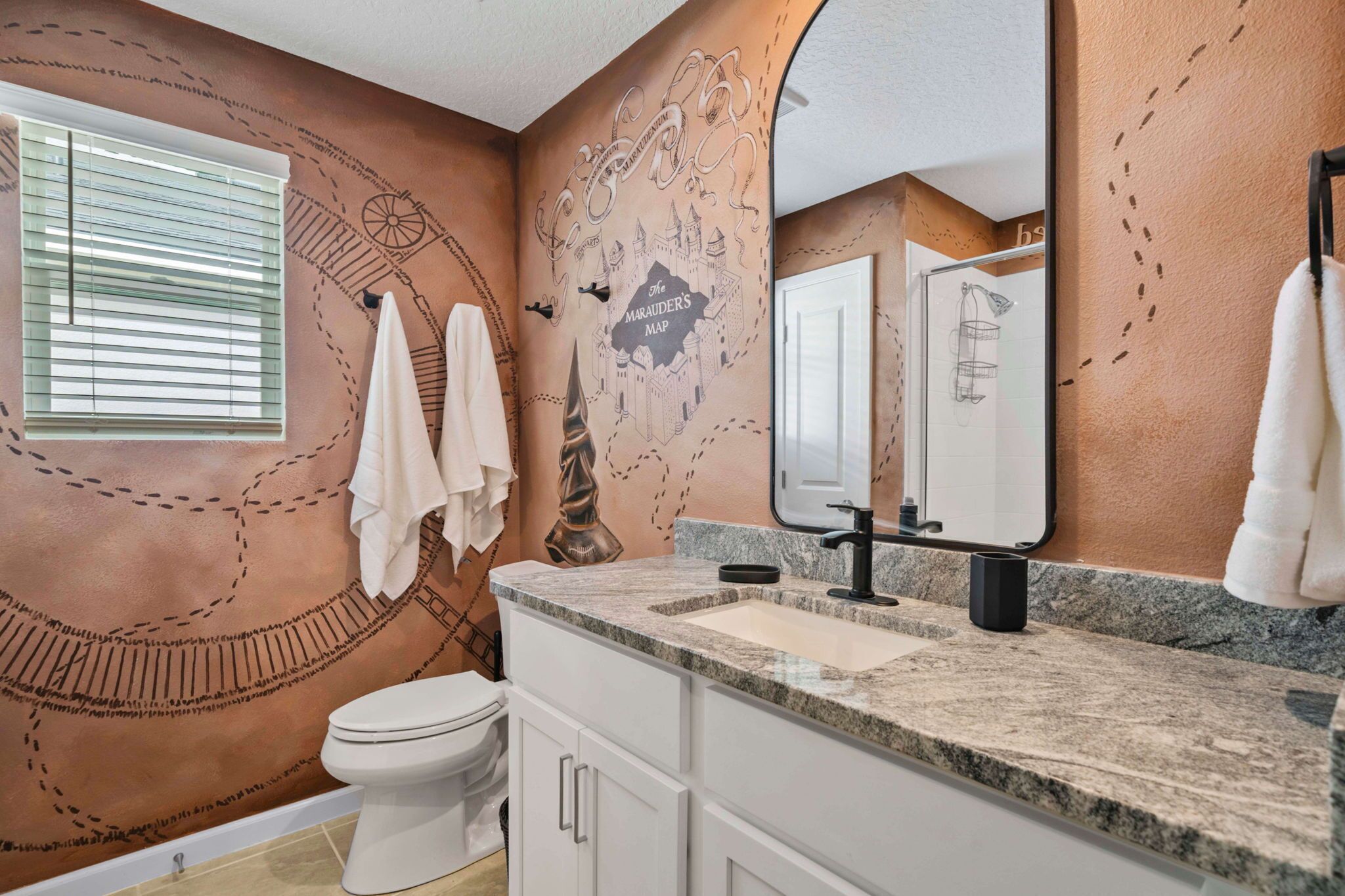 A bathroom with a large mirror, a sink, and a toilet. There is a towel rack with towels and a wall mural.