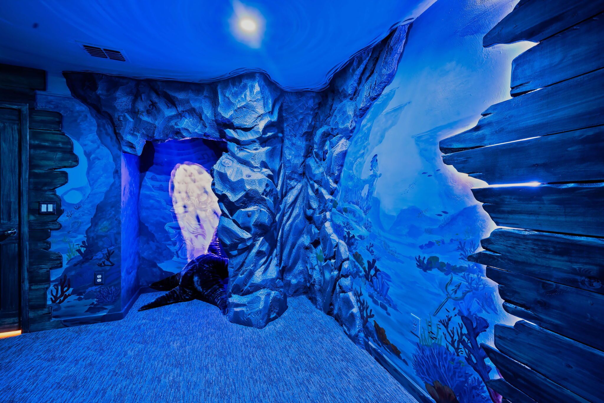 An aquarium with a large turtle, rocky walls, and a wooden floor.