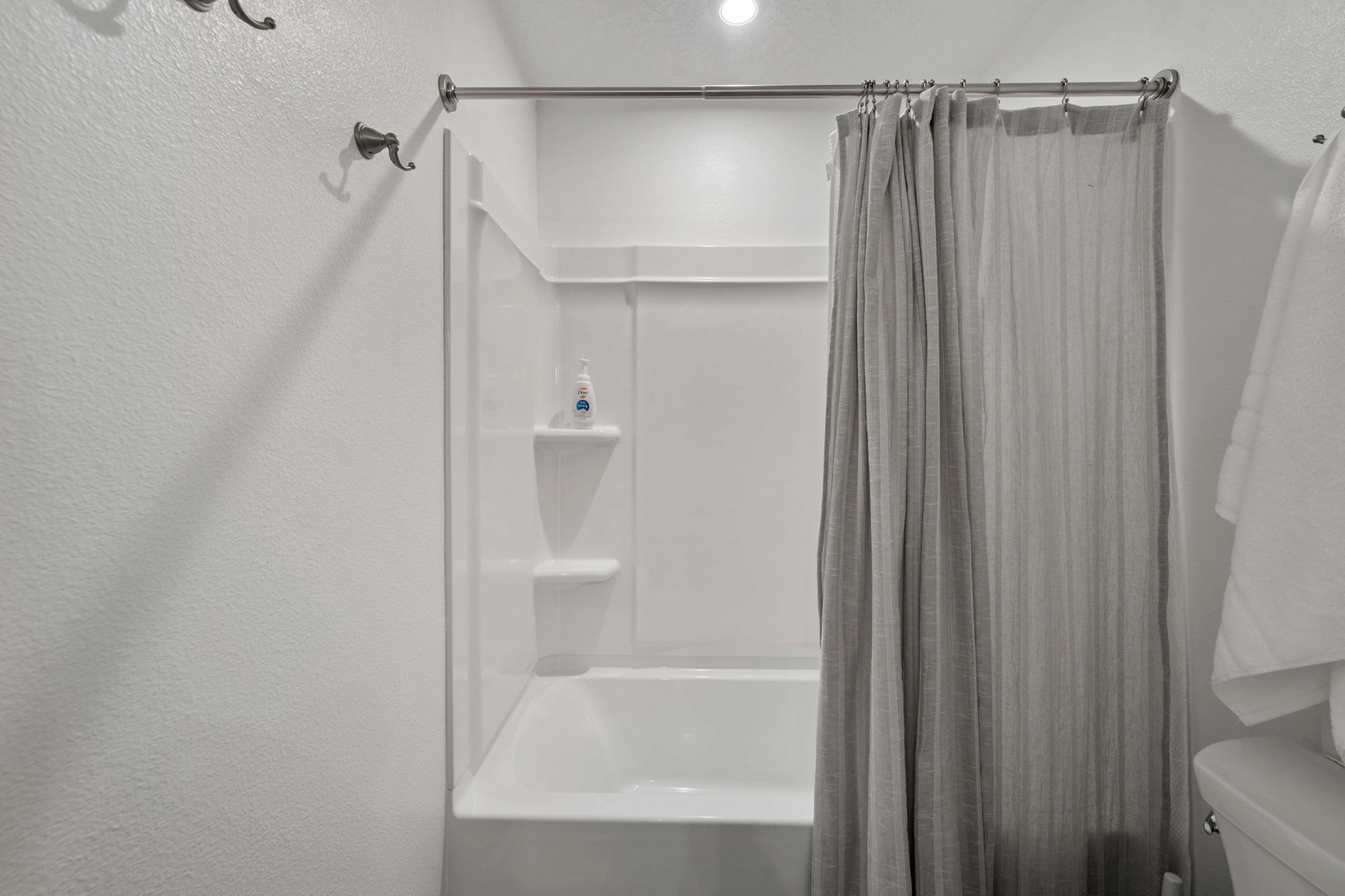 A bathroom with a shower, toilet, and a shelf with toiletries.