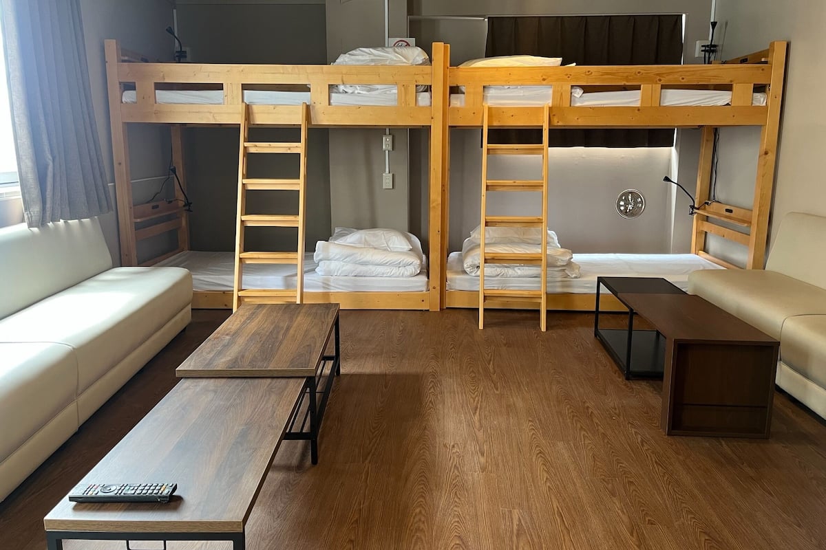 A bunk bed room with a wooden ladder, a sofa, a table, and a TV.