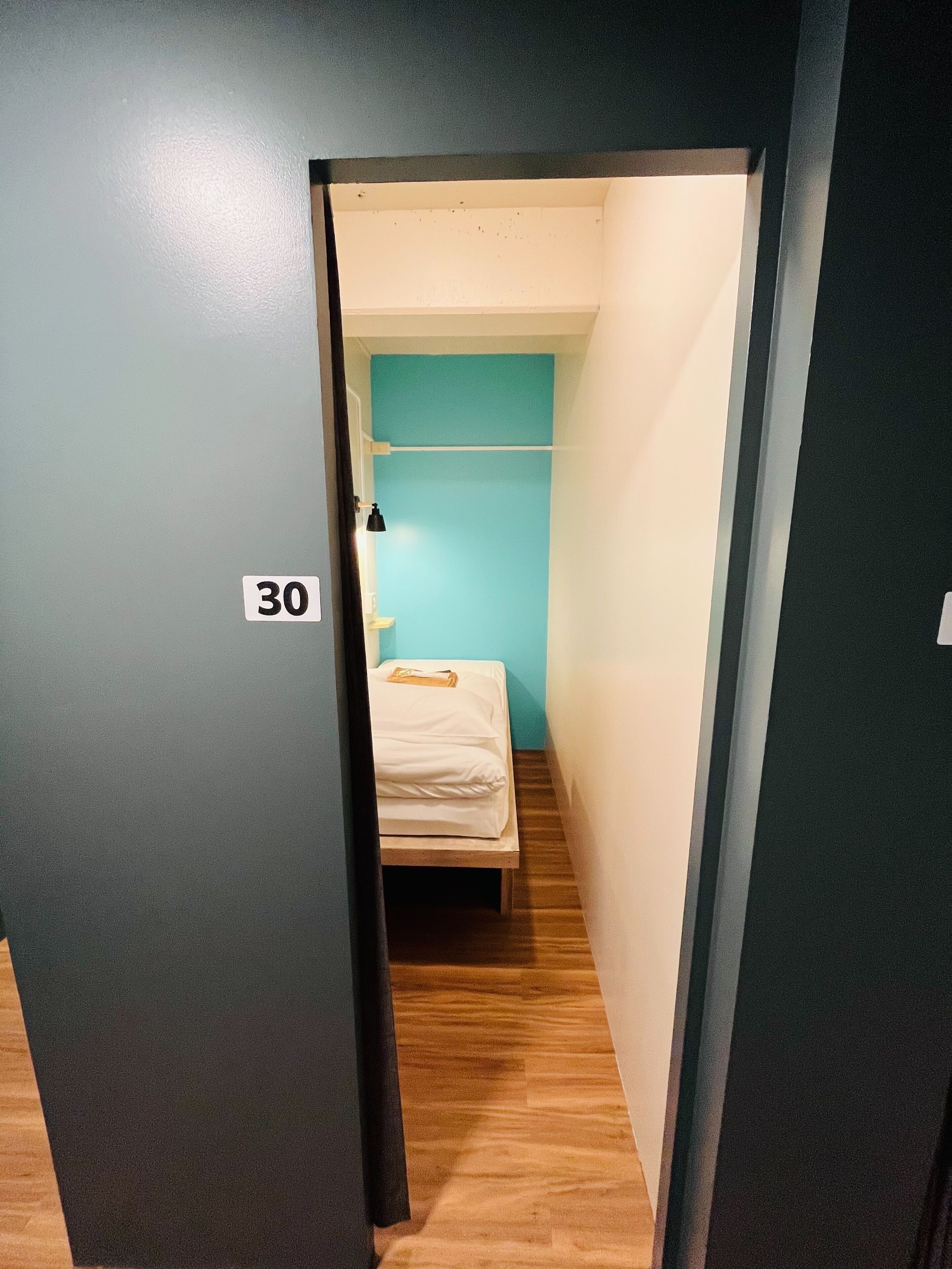 A narrow hallway leading to a small room with a bed and a blue wall.