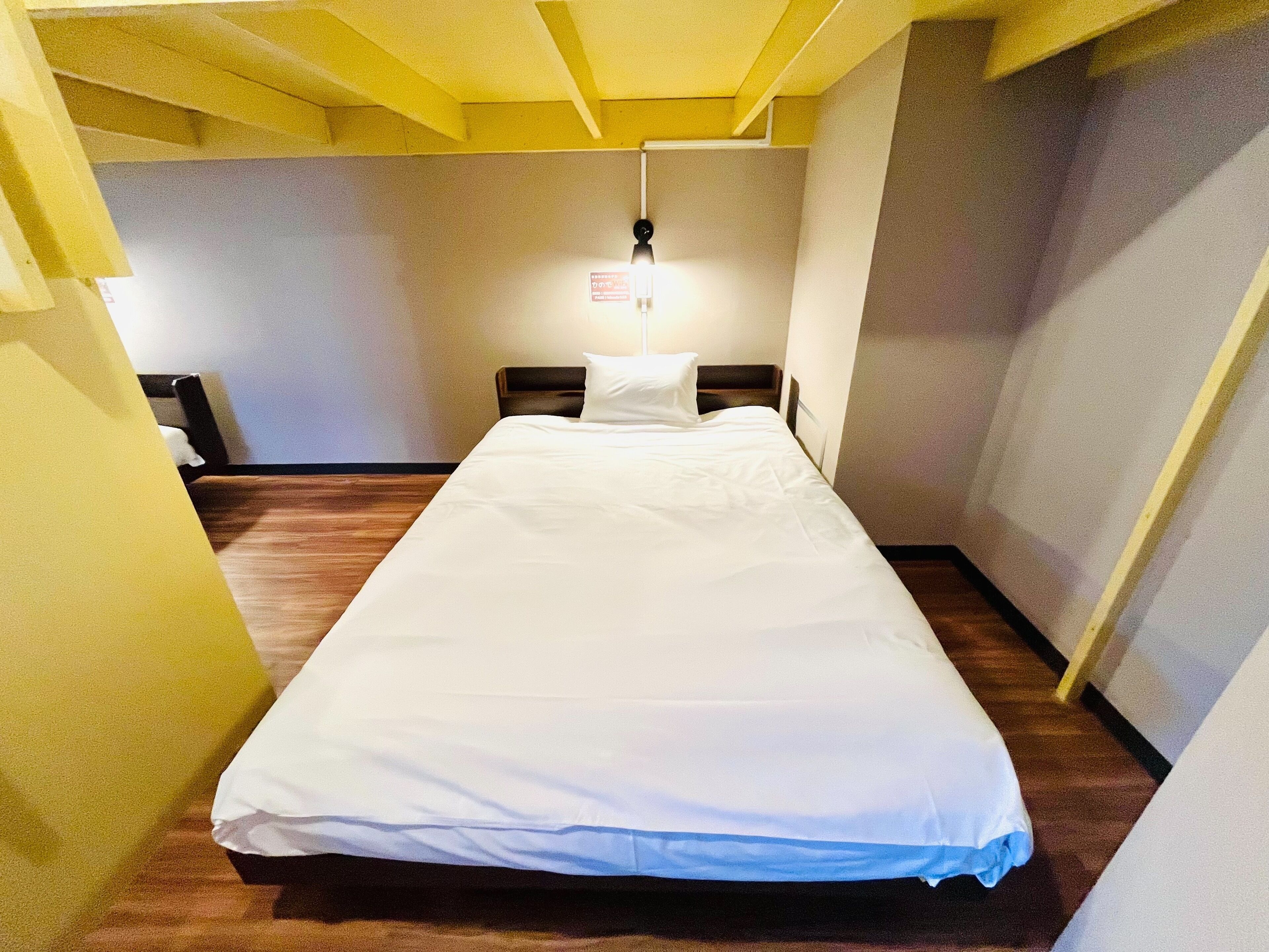 Una cama individual en una habitación con piso de madera y techo amarillo.