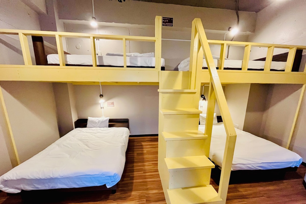 A dormitory room with bunk beds, a wooden staircase, and a white wall with a sign.