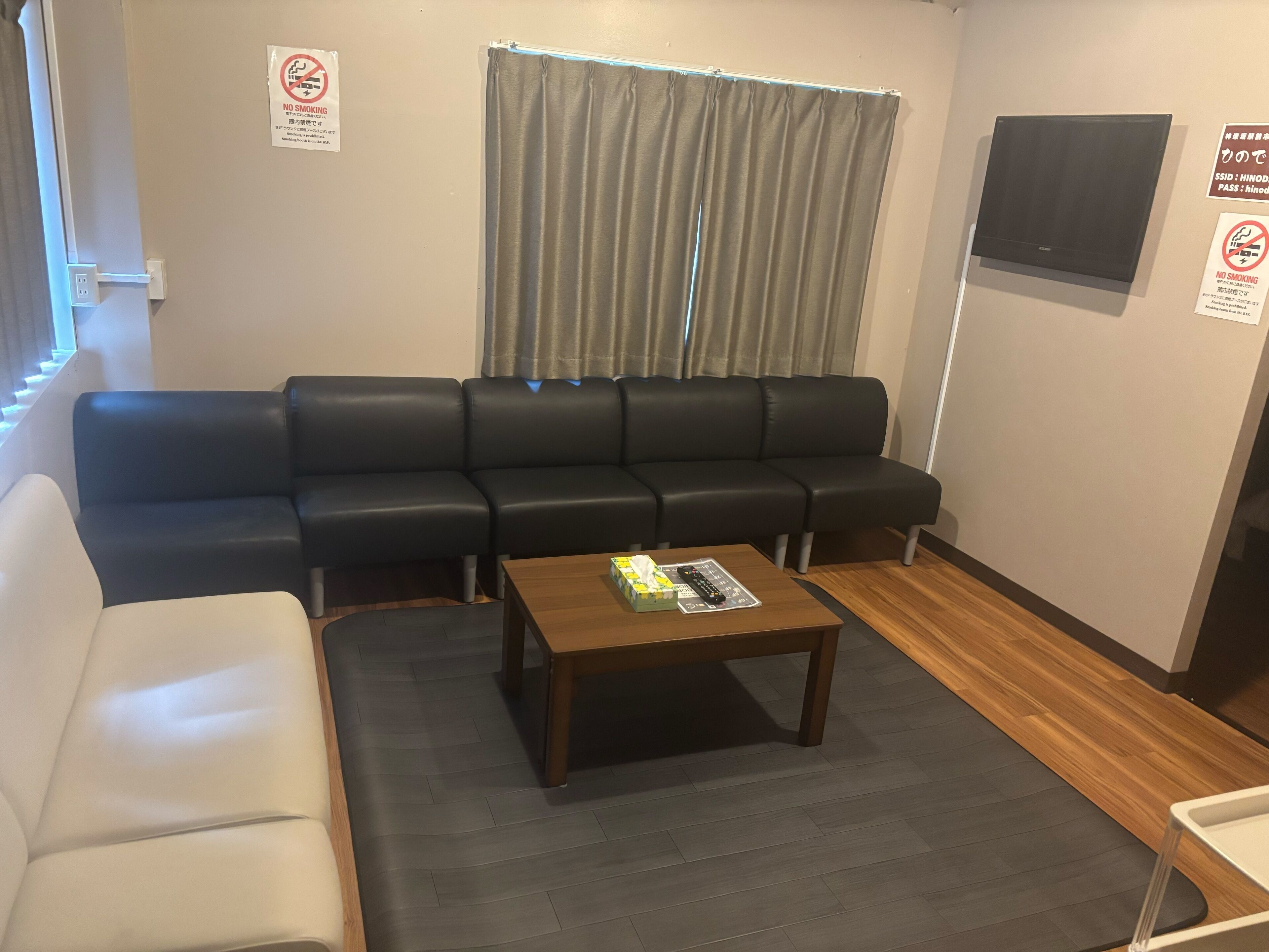 A seating area with a sofa and a table, a window with curtains, and a wall-mounted TV.
