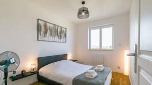 A bedroom with a bed, bedside fan, wall art, window, and radiator.