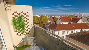 A balcony with a table and chairs, a potted plant, and a view of the cityscape.