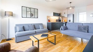A modern living room with a sofa, a coffee table, and a dining area with a kitchen in the background.