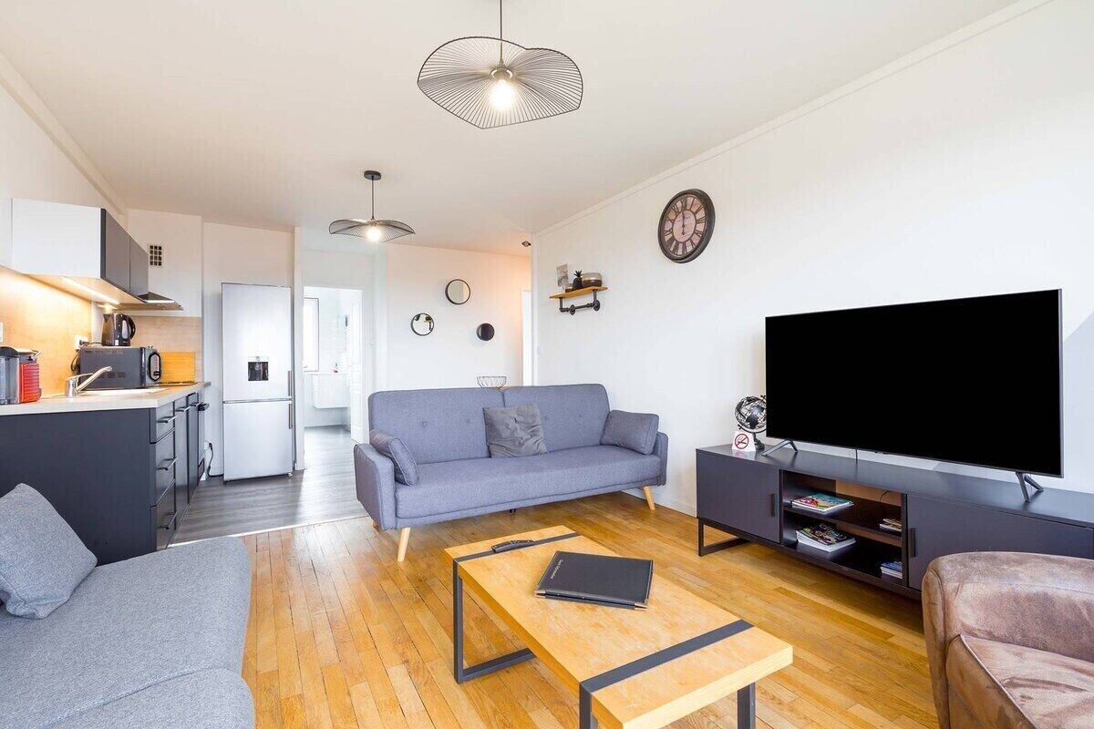 Un espace de vie moderne comprenant un canapé, une table basse, un téléviseur et un coin cuisine.