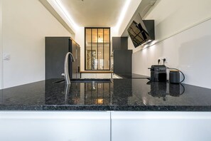 Effortlessly prepare meals in this kitchen with a sleek countertop, stainless steel faucet, and convenient coffee machine.