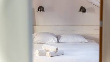 Una cama con ropa de cama blanca y dos toallas enrolladas, un cabecero de madera y dos lámparas fijadas a la pared.