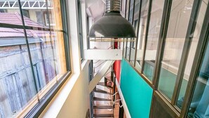Un escalier étroit avec un plancher en bois, une rampe en métal et un luminaire suspendu.