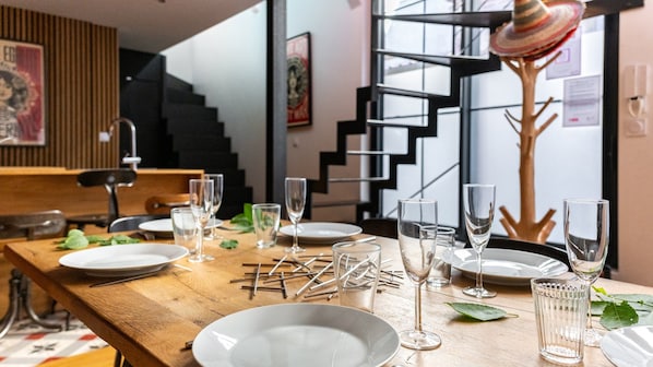 A dining table set with plates, glasses, and cutlery, with a staircase and a decorative wall in the background.
