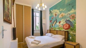 Un dormitorio con cama, mesita de noche, un cuadro y ventana con cortinas.
