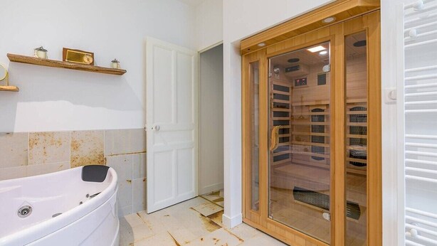 Un baño con una bañera, una puerta de madera y un estante con objetos.