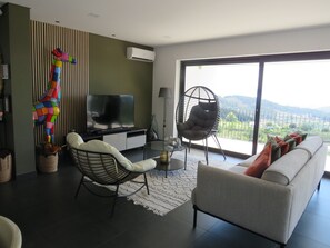 A modern living room with a sofa, two chairs, a television, and a large window with a view.