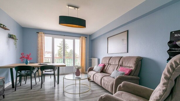 Una sala de estar con sofá, sillas, una mesa de centro, un lámpara colgante y una ventana con cortinas.