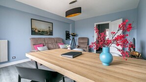 Una sala moderna con una mesa de comedor de madera, dos sofás, un jarrón azul con flores rojas y un cuadro en la pared.