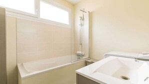 Un baño con bañera, ducha, lavamanos y ventana.