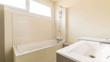 Een badkamer met een bad, douche, wastafel en raam.