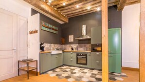 Une cuisine avec un sol à motifs hexagonaux, un réfrigérateur vert et une enseigne sur laquelle on peut lire : « LE BAR DE L’ESCAILLE ».