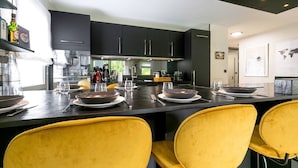 Een moderne keuken met donkere kastjes, een centraal eiland en gele stoelen.