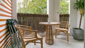 Een balkon met rieten meubilair, een potplant en uitzicht op bomen.