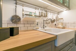 A modern kitchen with a white sink, wooden countertop, hanging pots, and a metal rack. - le Tillot (Dijon)