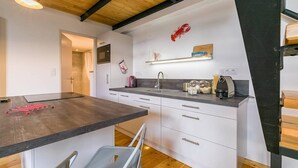 Uma cozinha moderna com uma ilha central, armários brancos e teto de madeira.