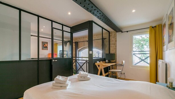Quarto de hotel com cama, escrivaninha, cadeira e janela com cortinas.