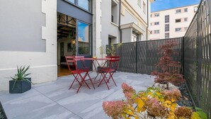 Um pátio com mesa e cadeiras, um vaso de planta e um jardim com arbustos.